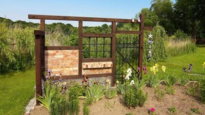 A rustic wooden gate with a brick wall, surrounded by a garden with various flowers and plants. - Ferienwohnung, Zemitz (Zemitz)