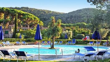 Un espace piscine agrémenté de chaises longues et de parasols, entouré de verdure et de collines.