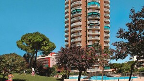 Un hotel alto de varios pisos con balcones, rodeado de árboles y una piscina.