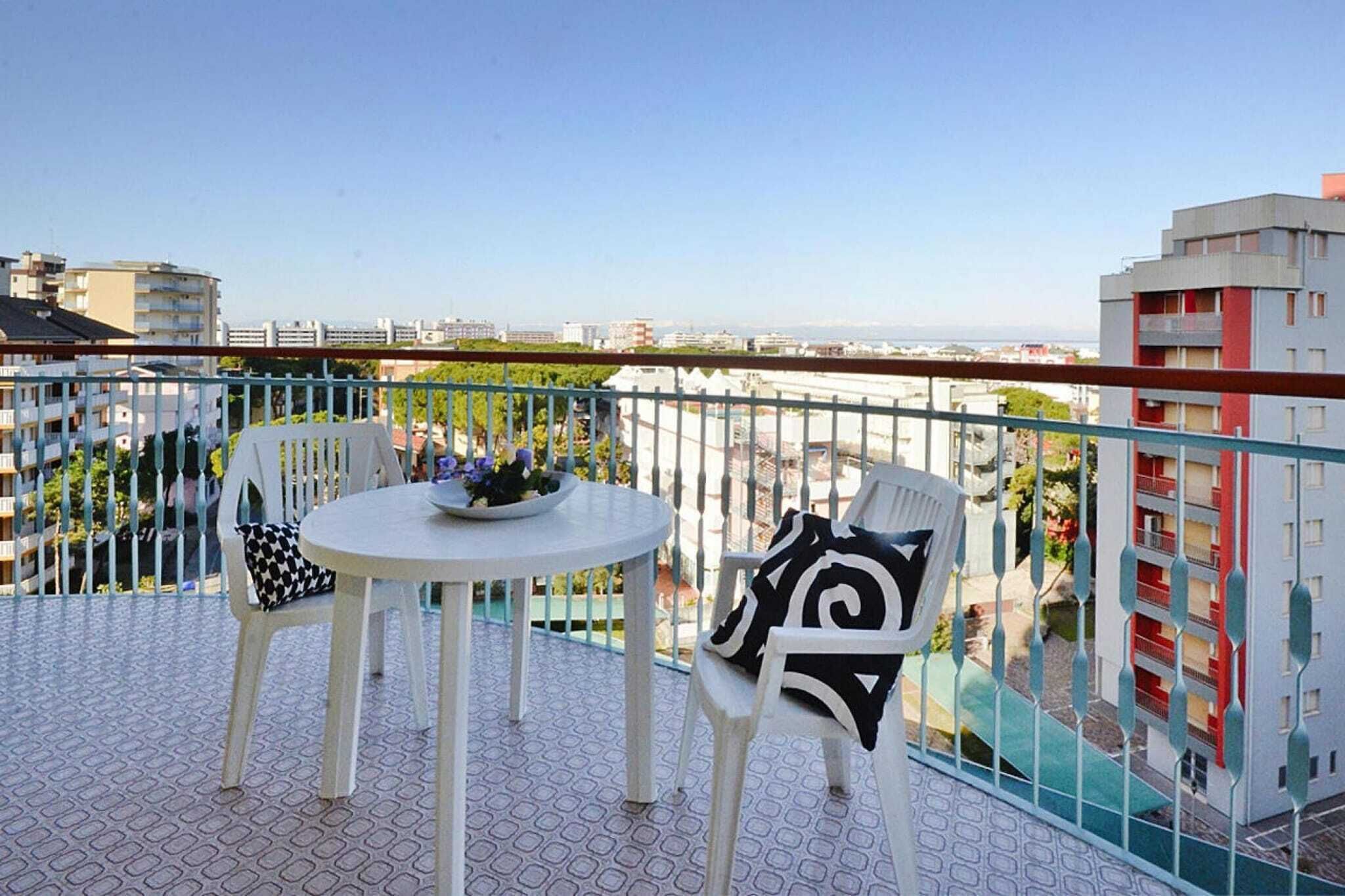 A balcony with a round table and two chairs, a railing, and a view of buildings and greenery.