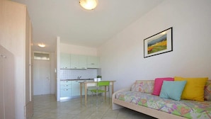Un espacio habitable compacto con kitchenette, zona de comedor y sofá con cojines de colores.