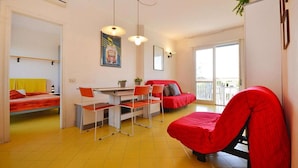Un espacio habitable compacto con cama, una mesa de comedor con sillas, un sofá rojo y un balcón con vistas.