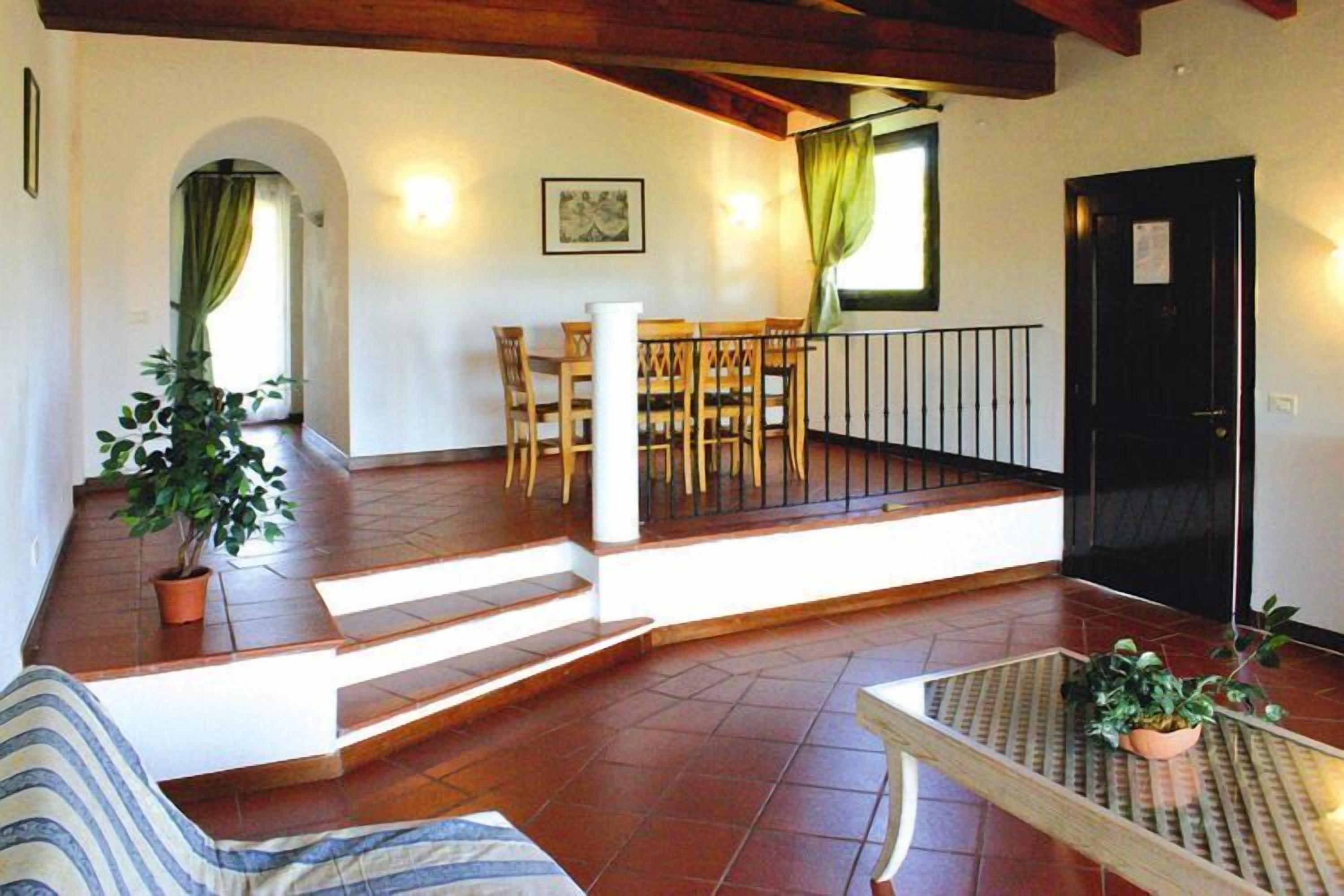 A spacious living area with a wooden staircase, a dining table with chairs, and a black door.
