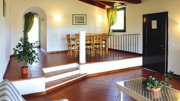 A spacious living area with a wooden staircase, a dining table with chairs, and a black door.