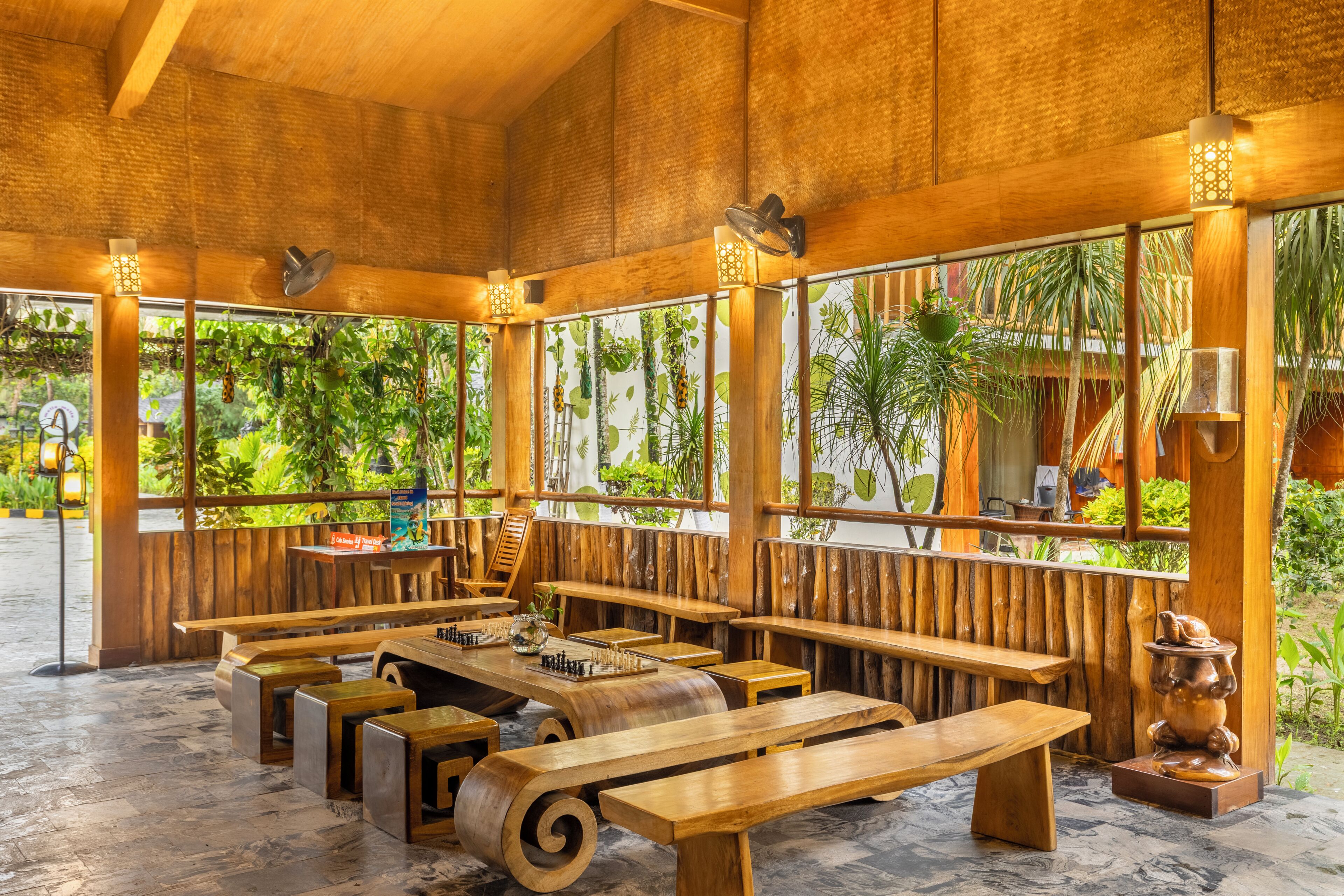A wooden interior with multiple seating areas, including benches and tables, and large windows with views of greenery.