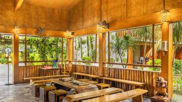 A wooden interior with multiple seating areas, including benches and tables, and large windows with views of greenery.