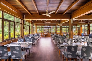A spacious indoor dining area with wooden beams, large windows, and tables set for dining. - TSG Blue Resort and Spa (Port Blair)