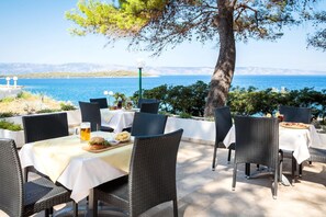 Un espace extérieur aménagé pour prendre les repas, avec des chaises et des tables en osier, une chope de bière et un hamburger sur un plateau.
