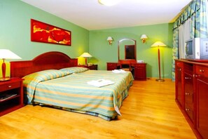 Une chambre d’hôtel avec un lit, des tables de chevet, un bureau, un miroir, une télévision et un tableau au mur.