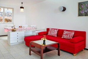 A red sofa with zebra-patterned pillows, a white coffee table with a vase, and a white desk with chairs. - Elegant Resort Stay for 4 in Jelsa (Jelsa)