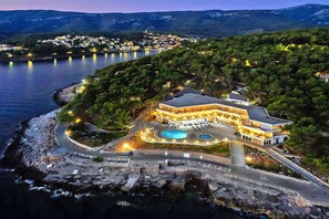 Un hôtel situé sur la côte, doté d’une piscine, entouré d’arbres et offrant une vue sur une étendue d’eau.