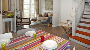 A dining area with a striped tablecloth, a sofa, and a staircase.