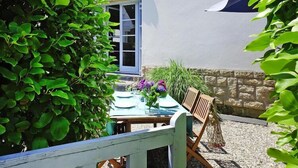 An outdoor dining area with a table set for two, surrounded by greenery and a stone wall.