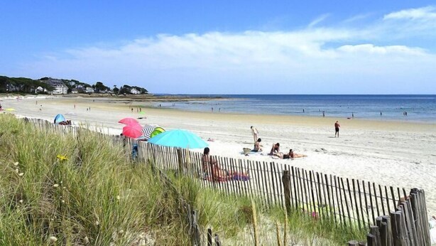 A beach with a wooden fence, umbrellas, and people relaxing.