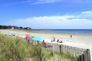 A beach with a wooden fence, umbrellas, and people relaxing. - Holiday Home in Carnac near Sandy Beach (Carnac)