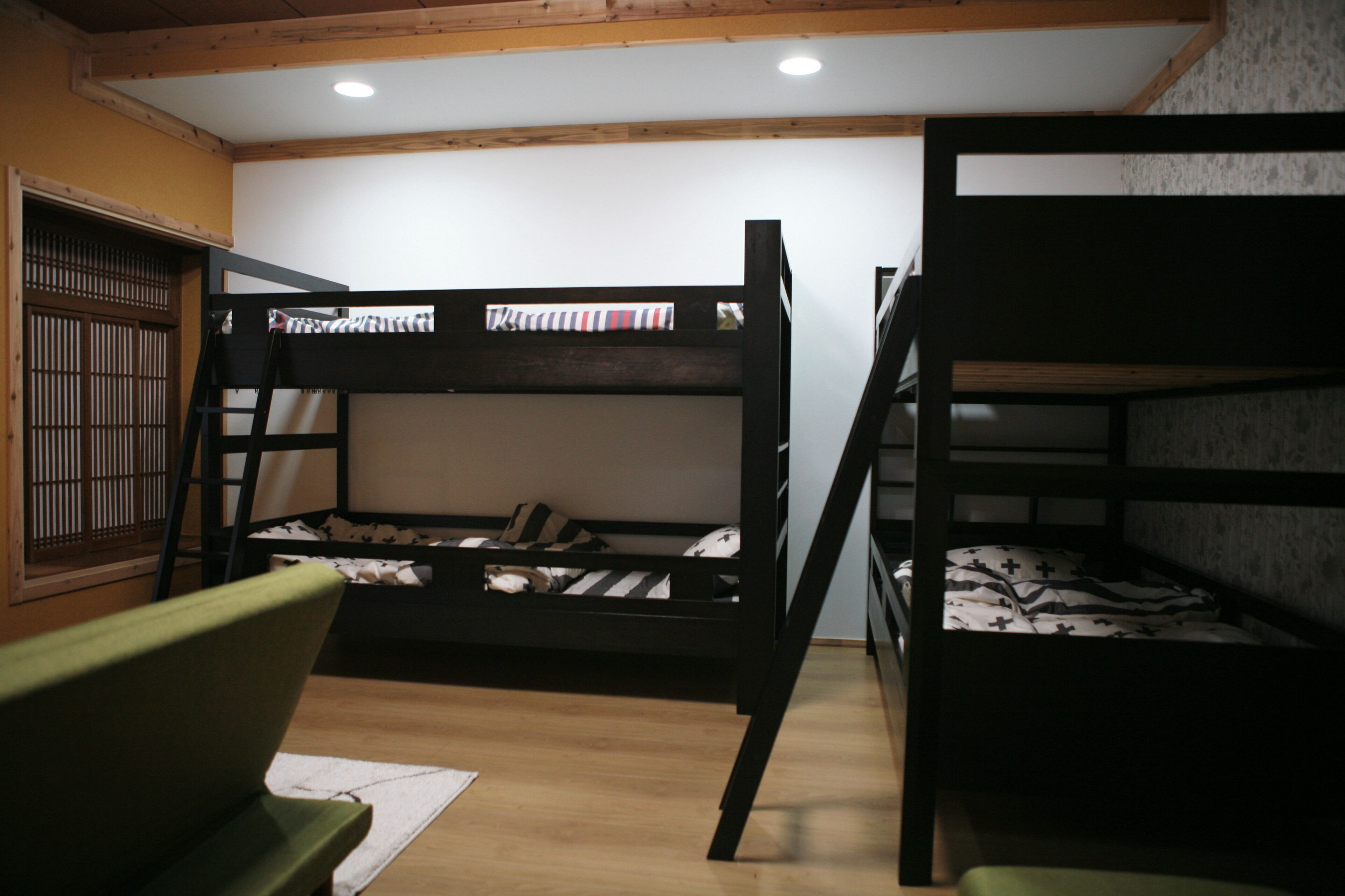 A bunk bed room with a wooden ladder, a green chair, and a futon bed.