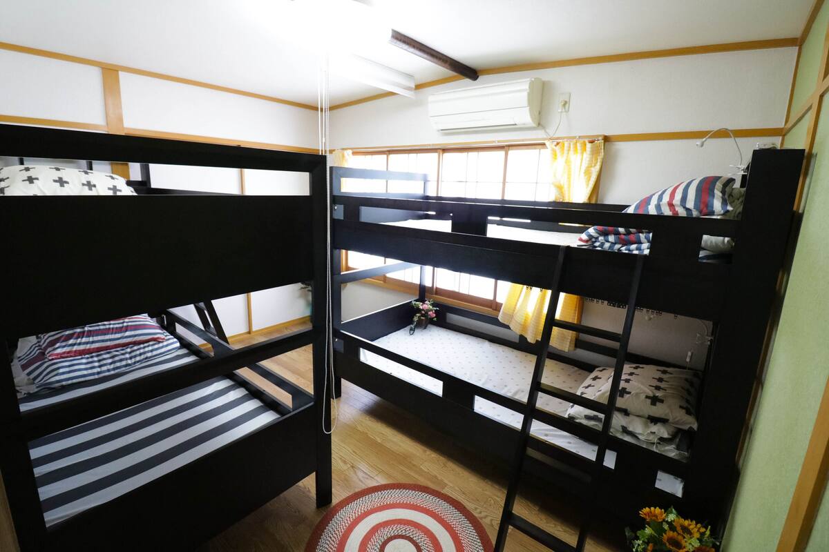 Habitación con literas, suelo de madera, una alfombra pequeña y una ventana con cortinas.