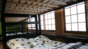 A bunk bed with a white and black cross-patterned bedspread, wooden beams on the ceiling, and large windows with wooden frames. - Maru House - Hostel (Osaka)