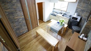 A compact kitchen with a wooden table, a bench, and a microwave. - Maru House - Hostel (Osaka)