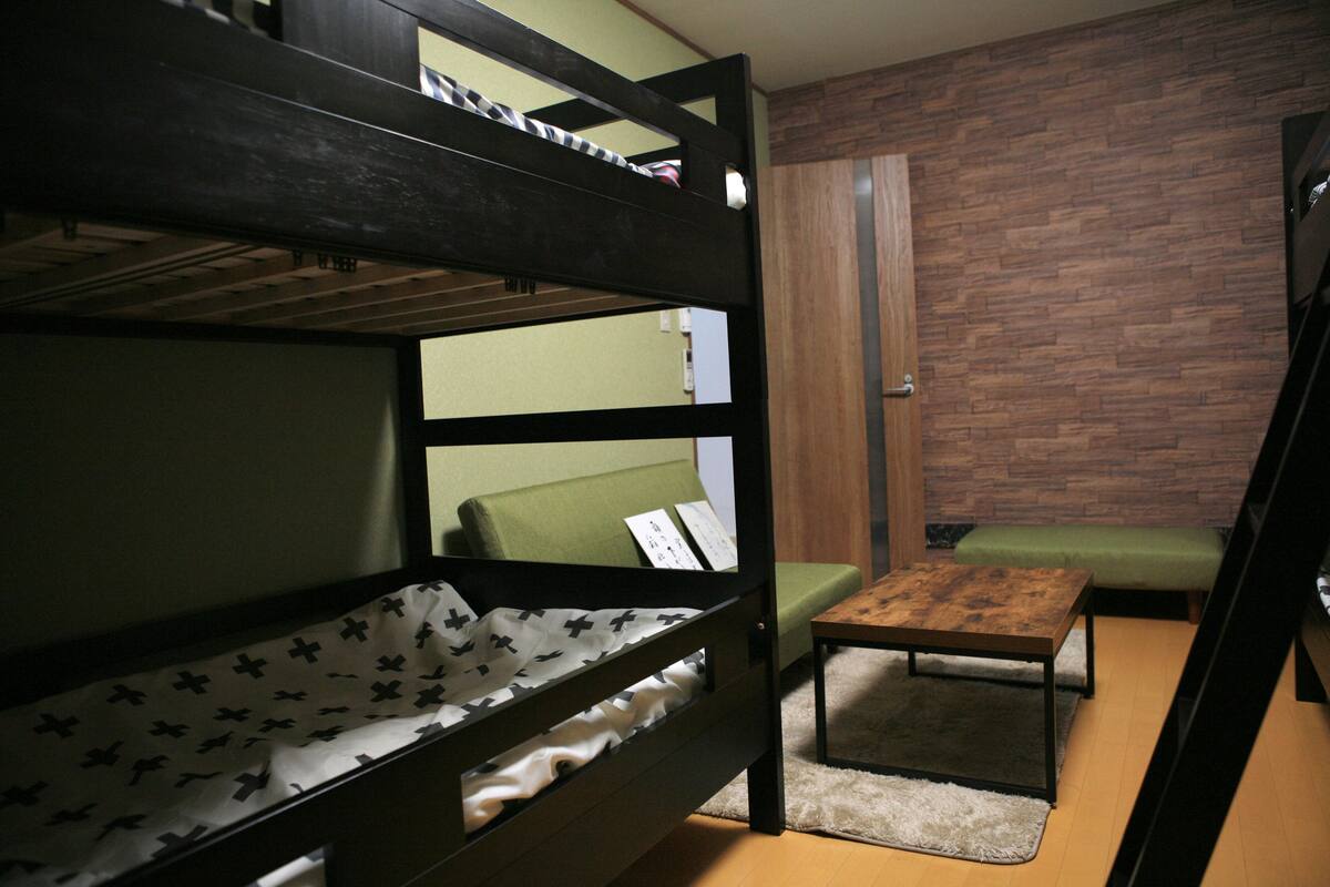 Una cama litera con un cojín verde y una pequeña mesa de madera en una habitación con pared de ladrillo.
