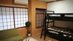 A room with a bunk bed, a sofa, a small table, a potted plant, and a sliding door. - Maru House - Hostel (Osaka)