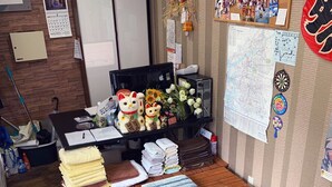 A small office with a desk, computer, and various items including towels, a teddy bear, and a map. - Maru House - Hostel (Osaka)