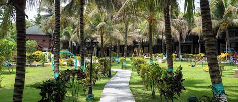 A pathway lined with palm trees and small shrubs, leading to a building with a dark facade.