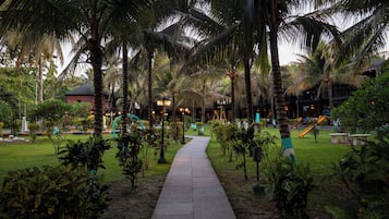 A pathway leading through a garden with palm trees and a playground.