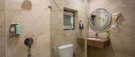 A bathroom with a glass-enclosed shower, a toilet, a sink with a mirror, and toiletries on the wall.