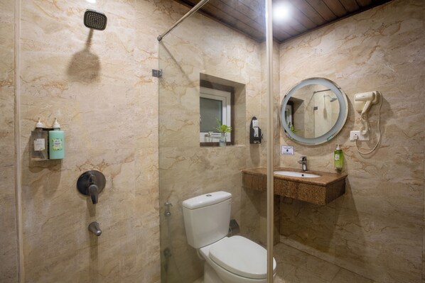 Uma casa de banho com cabine de duche em vidro, sanita, lavatório com espelho e produtos de higiene pessoal na parede.