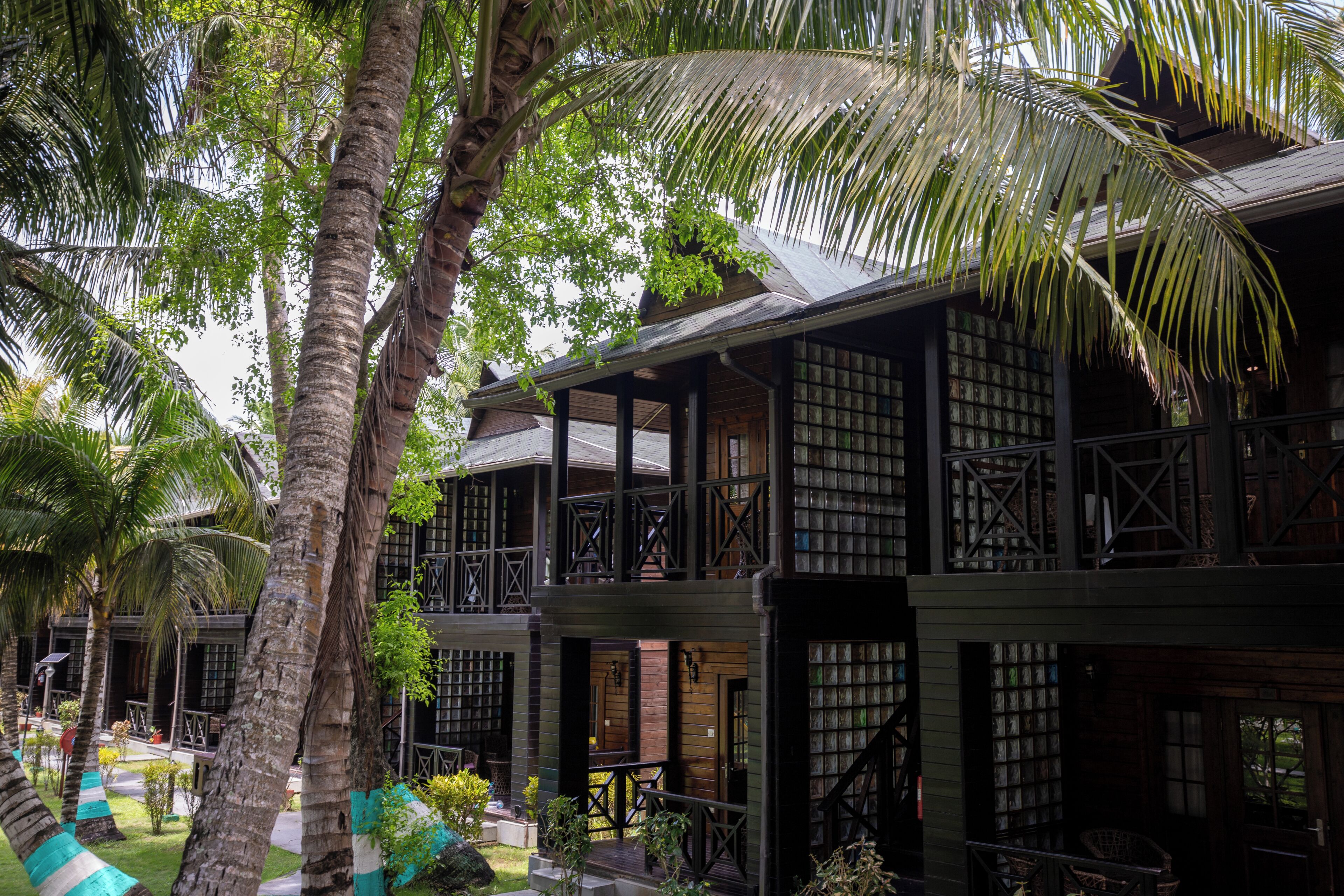 A traditional wooden building with multiple balconies, surrounded by lush greenery and palm trees.
