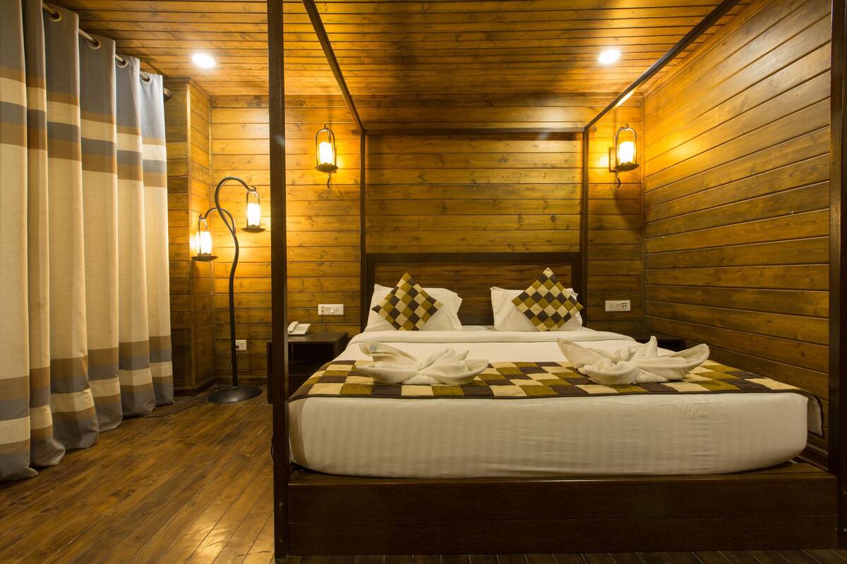 Una habitación con paneles de madera, una cama, dos luces fijadas a la pared y una mesita de noche con un teléfono.