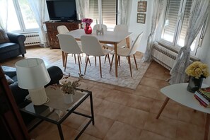A living room with a TV, dining table, chairs, sofa, and a coffee table with a lamp and flowers. - Holiday Home in Benissa by Cala Advocat Bay (Benissa)