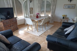 A living room with a TV, sofa, dining table, chairs, and a small side table with a lamp. - Holiday Home in Benissa by Cala Advocat Bay (Benissa)