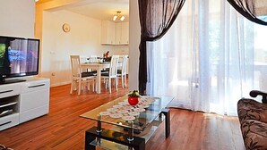Un salon avec une table basse en verre, un téléviseur et un coin repas comprenant des chaises et une table.