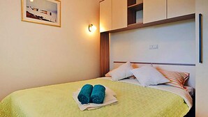 Un lit bien fait, recouvert d’une couette verte, avec deux serviettes enroulées et un tableau encadré accroché au mur.
