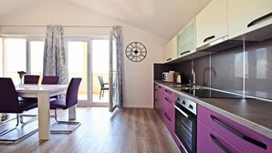 Une cuisine moderne dotée d’appareils électroménagers en acier inoxydable, un coin repas avec des chaises violettes et une grande fenêtre agrémentée de rideaux.