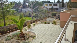Un balcon doté d’un sol carrelé, entouré d’un jardin où poussent différentes plantes et un palmier.