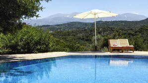 A swimming pool with a wooden chair and umbrella, surrounded by greenery and mountains in the background. - Romantic Holiday Home in Drosia (Drosia)