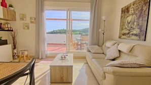 Una sala de estar moderna con un sofá, una mesa de centro y un cuadro de Buda. Hay un balcón con vistas a las colinas.