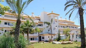 Un hotel de varios pisos con fachada blanca y detalles amarillos, rodeado de palmeras y un césped cuidado.