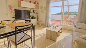 Una sala de estar moderna con una mesa de vidrio, un sofá, un televisor y un balcón con mobiliario exterior.