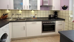 A compact kitchen with a washing machine, a stove, and a sink. - Gemütlicher Bungalow Kabeljau in Dornumersiel (Dornumersiel)