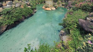 A clear, turquoise stream surrounded by rocks and greenery, with a modern building in the background. - Jin Yong Quan Spa Hotspring Resort (New Taipei City)