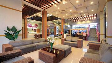 A spacious lobby with a modern design, featuring a central seating area with sofas and a coffee table, surrounded by wicker furniture.