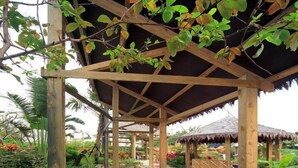 A covered swimming pool with a wooden pavilion, surrounded by tropical plants and rocks. - Jin Yong Quan Spa Hotspring Resort (New Taipei City)