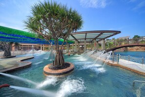 Una fuente de agua con un árbol central, una piscina y una zona cubierta con techo de cristal.