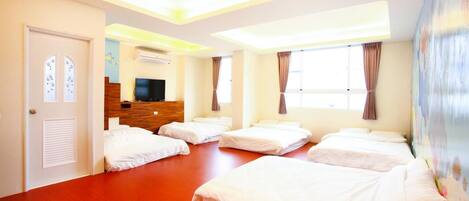 A hotel room with four beds arranged in a row, a TV, and a wooden headboard.