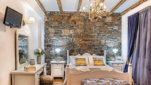 A bedroom with a stone wall, a bed with pillows, a bedside table, a TV, and a chandelier. - Private Pool & Garden Villa for 6 (Pemonia)