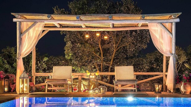 A poolside area with a wooden pergola, two lounge chairs, a table with a lamp, and a clear blue pool. - Private Pool & Garden Villa for 6 (Pemonia)